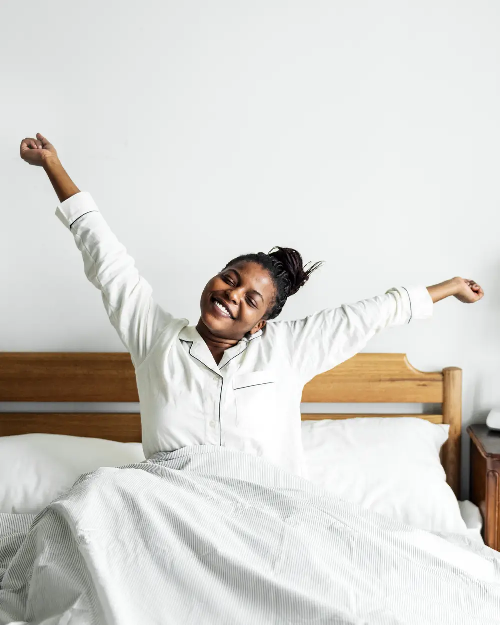 A vendor stretches both arms wide as she wakes in a bright white bedroom, smiling