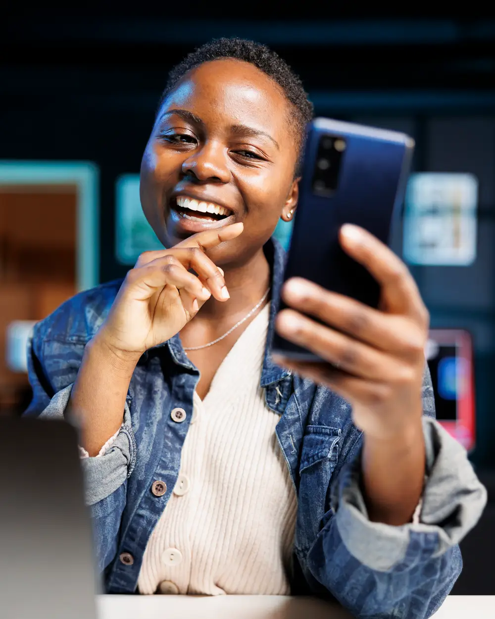 A boutique owner laughs as she talks to her phone, held up in front of her, in her shop at night